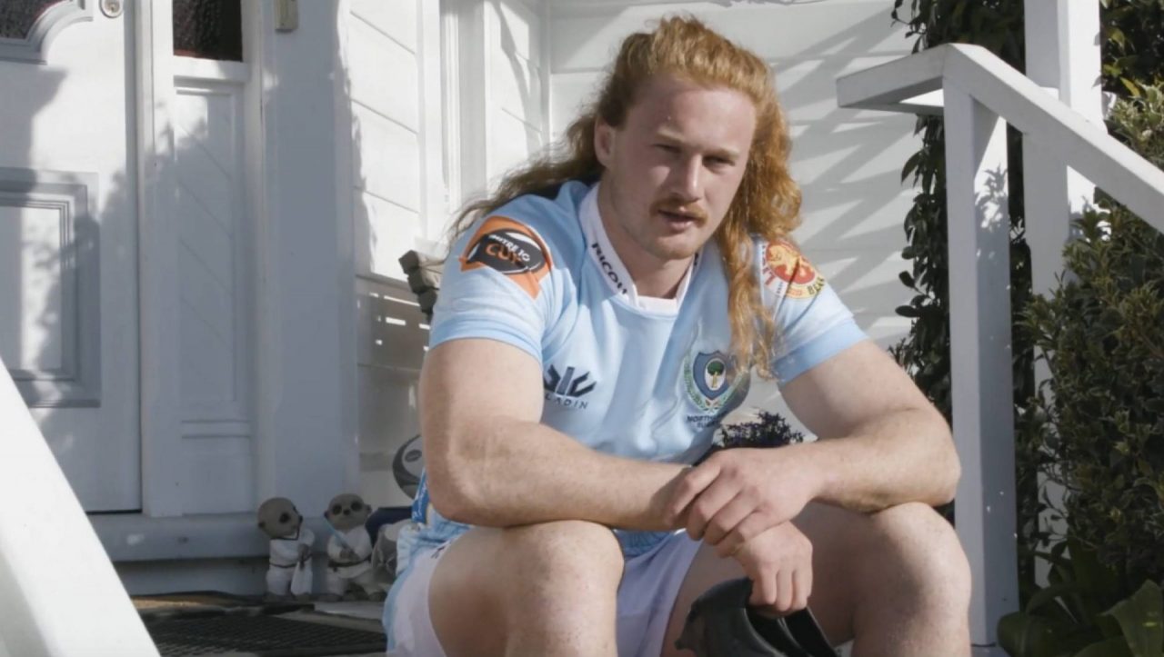 Northland Rugby player Tom Robinson sitting on front deck holding boots